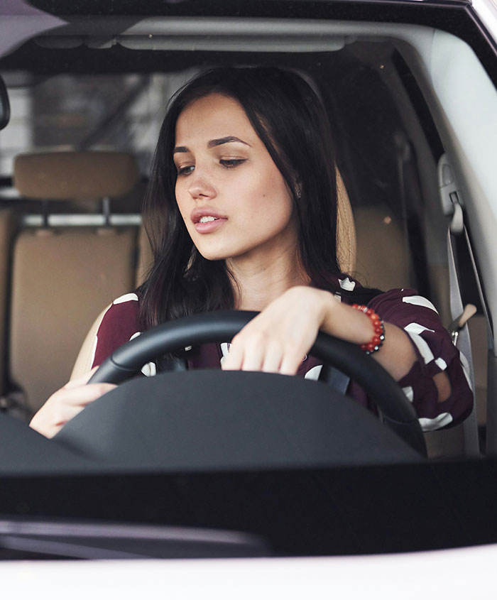Young woman sitting in a car looking down, capturing a moment related to popping the question and ring embarrassment.