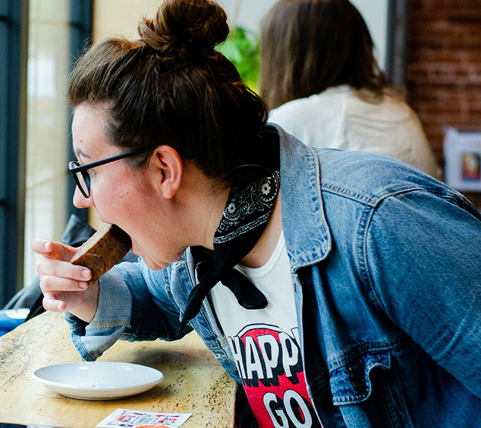 Person in denim jacket and black glasses eating at café, illustrating awkward moments when people popped the question.