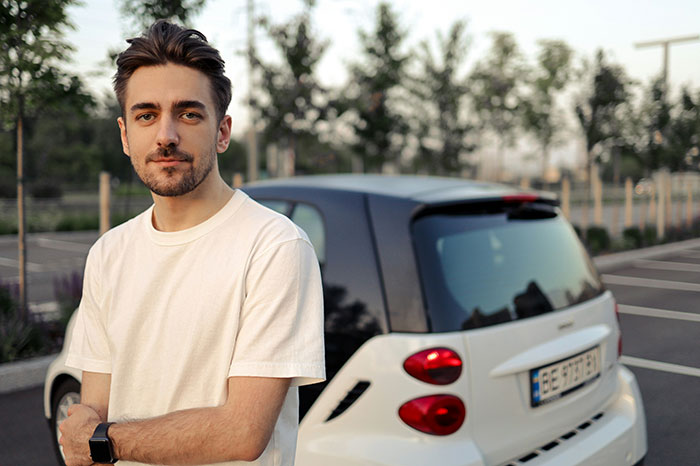 Young man standing by a car in a parking lot, reflecting on moments people popped the question with embarrassment.