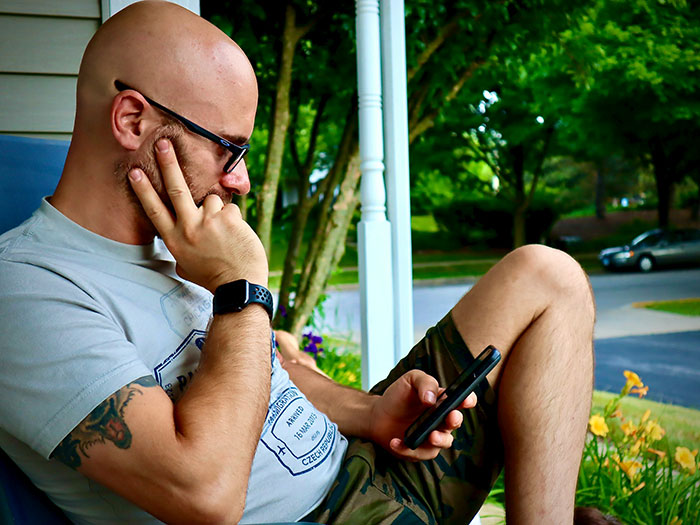 Man sitting outdoors, looking thoughtful and holding a phone, reflecting on moments of popping the question and embarrassment.