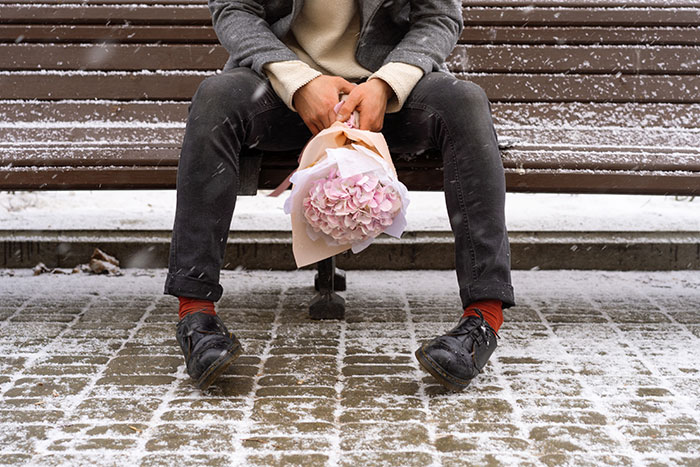 Man sitting on snowy bench holding bouquet, illustrating moments when people popped the question but faced embarrassment.