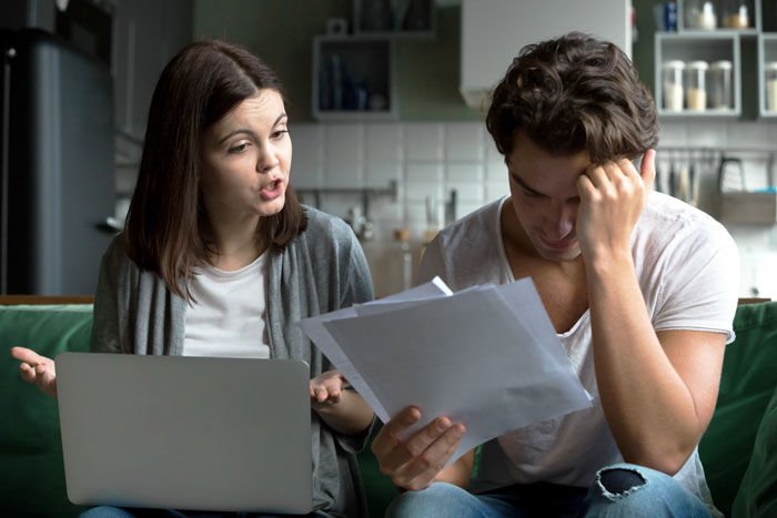 Couple in a tense discussion at home, woman explaining while man reviews documents, reflecting wedding gift conflict debate.