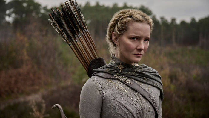 Female archer from The Rings Of Power Season 3, wearing medieval attire with a quiver of arrows, in a forest setting.
