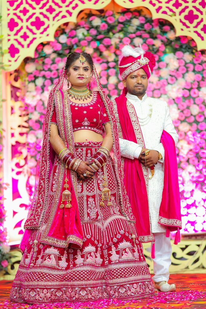 Bride and groom in traditional attire posing in front of a floral backdrop during a family tradition ceremony.