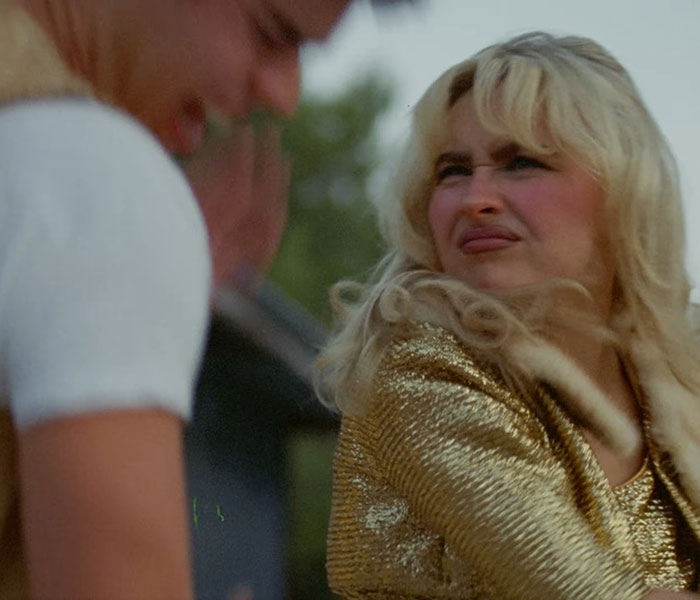 Sabrina Carpenter in a gold outfit showing a strong expression, spotlight on disturbing patterns in her music videos.