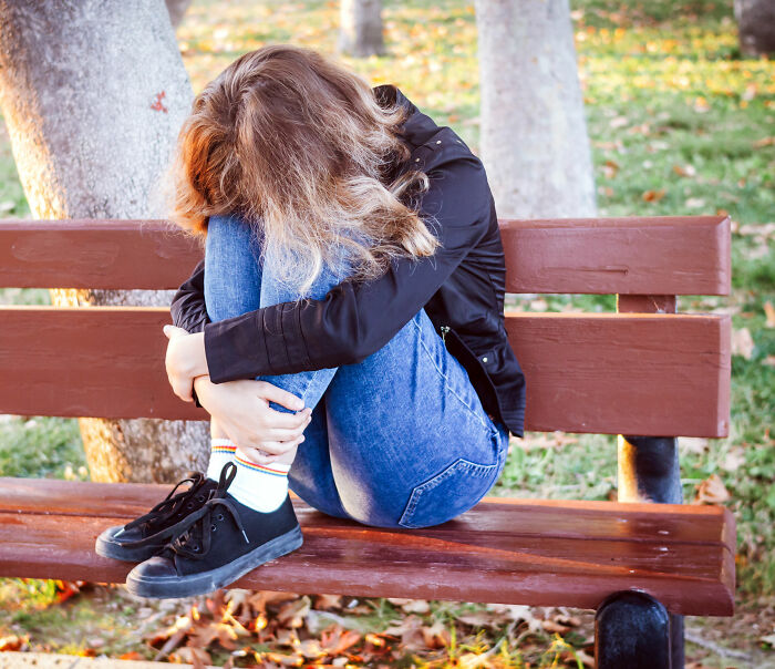 Teen girl sitting alone on a park bench looking distressed, related to mom arrested after leaving her at Universal Studios.