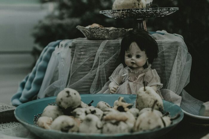 Creepy vintage doll sitting on a table with a bowl of decayed fruit, evoking terrifying urban explorer moments.