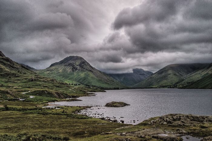 Scenic view of a lake surrounded by green hills under dramatic cloudy sky, illustrating mansplaining challenges in nature.