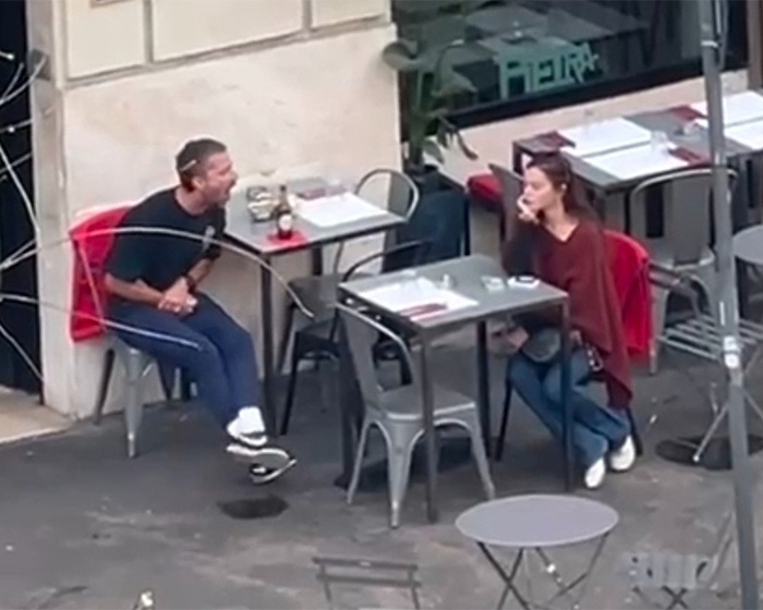 Shia LaBeouf sitting outdoors shouting at a woman across cafe tables in Rome during a heated argument.