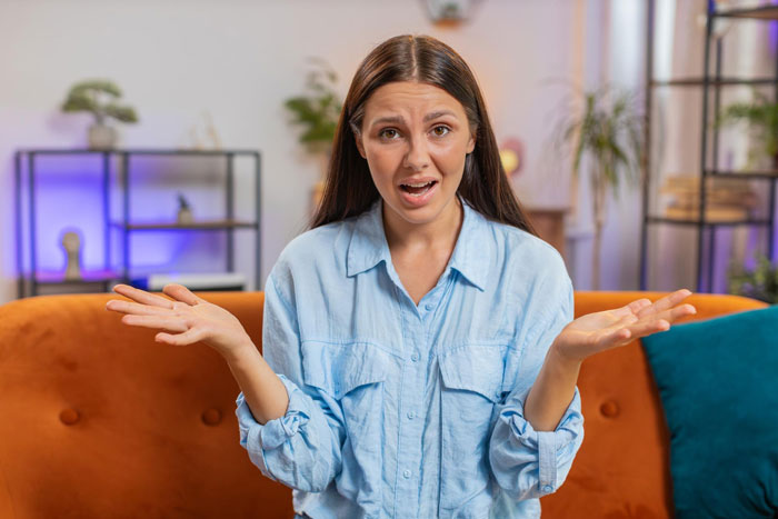 Young woman in a blue shirt sitting on a couch looking confused about a sil baby rude relationship issue indoors