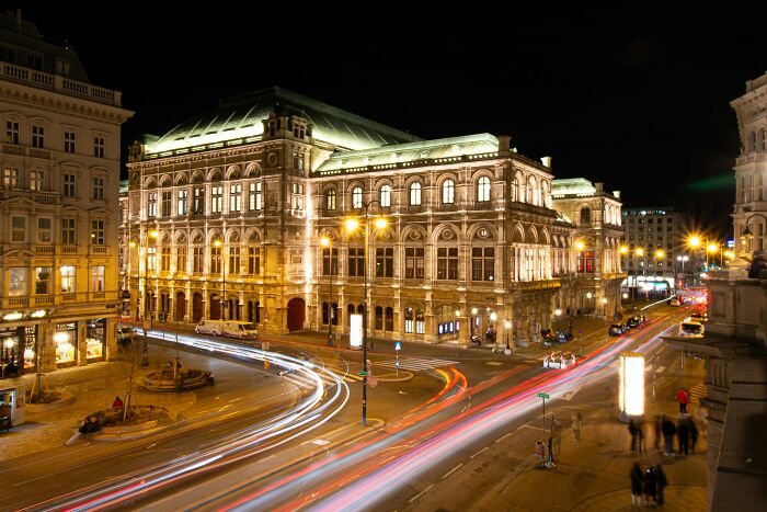 Historic illuminated building at night with busy street showing light trails, reflecting vanished truths from home countries.