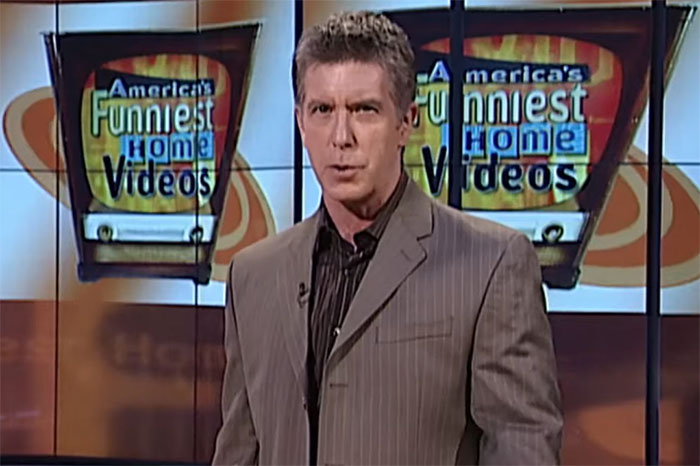Man in suit standing in front of screens showing America's Funniest Home Videos, evoking childhood memories.