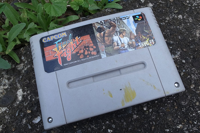Retro video game cartridge lying on ground surrounded by plants, evoking childhood memories and nostalgia.