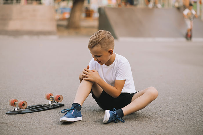 Young boy sitting on pavement holding his knee next to a skateboard, evoking childhood memories and playtime moments.