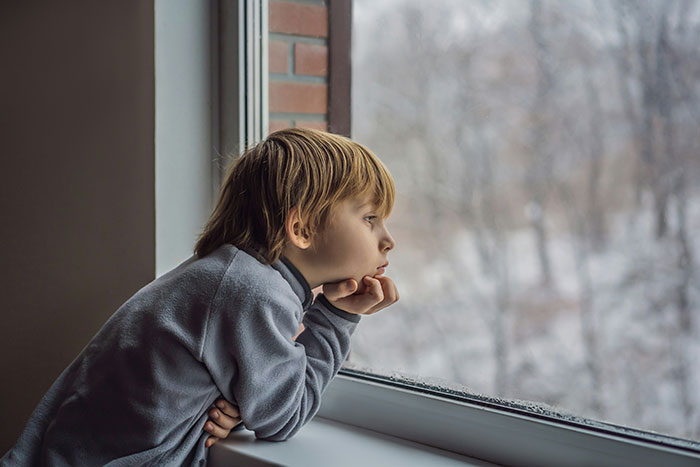 Young child gazing thoughtfully out a window, reflecting on childhood memories that might unlock your own memories.