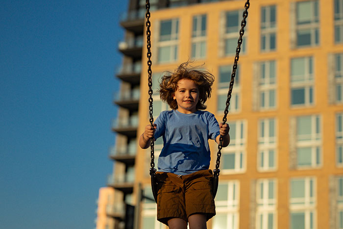 Child smiling on a swing outdoors with a building background, capturing moments that unlock childhood memories.