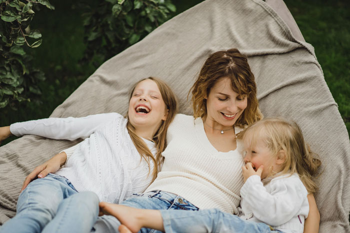 Mom and her two daughters relaxing outdoors on a blanket, highlighting co-parenting and free sitter responsibilities.