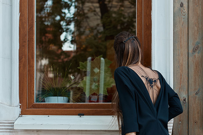 Woman with long hair and black dress looking through a window, symbolizing a sister catching her brother with secret boyfriend.