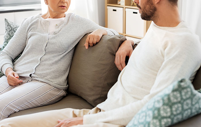 Older woman confronting young man on couch, capturing tense moment related to guy&rsquo;s sister catching secret boyfriend situation.