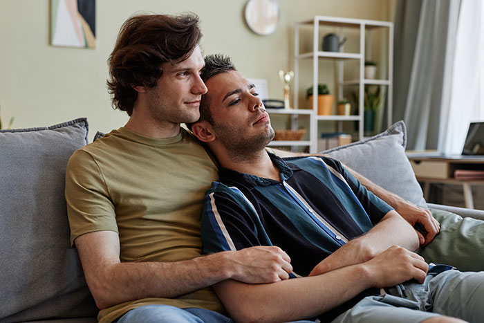 Two men sitting closely on a couch, showing affection and comfort in a cozy living room setting.