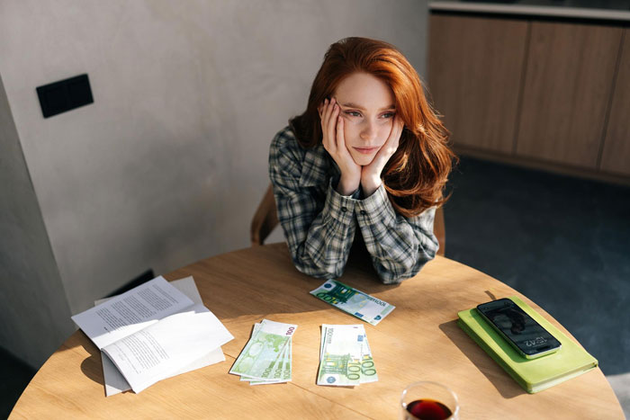 Teen girl sitting at table with euro bills and documents, appearing stressed about parents demanding sacrifice for sixth baby miracle.