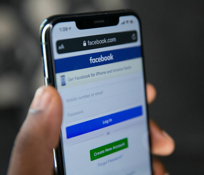 Person holding smartphone displaying Facebook login page, related to bodies of father and daughter found after PS5 purchase.