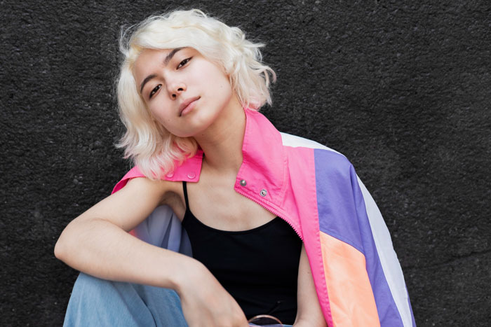 Young woman with blonde hair wearing a colorful jacket looking confident, portraying internet stranger living with boyfriend's family.