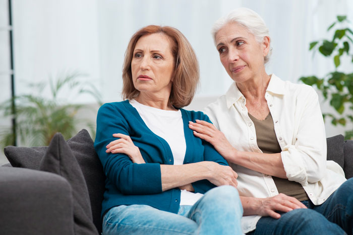Two women on a couch looking upset, depicting tension as a stranger starts living with boyfriend&rsquo;s family.