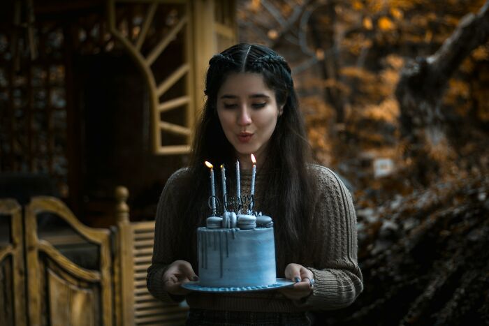 Young woman outdoors blowing candles on a cake, illustrating weird and unhinged family traditions celebration ideas.