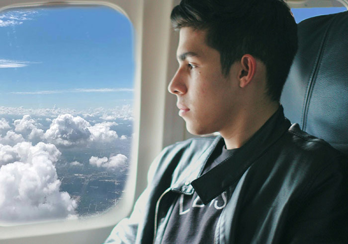 Young man wearing a leather jacket sitting on an airplane, looking thoughtfully out the window at the clouds, spoiled moment.