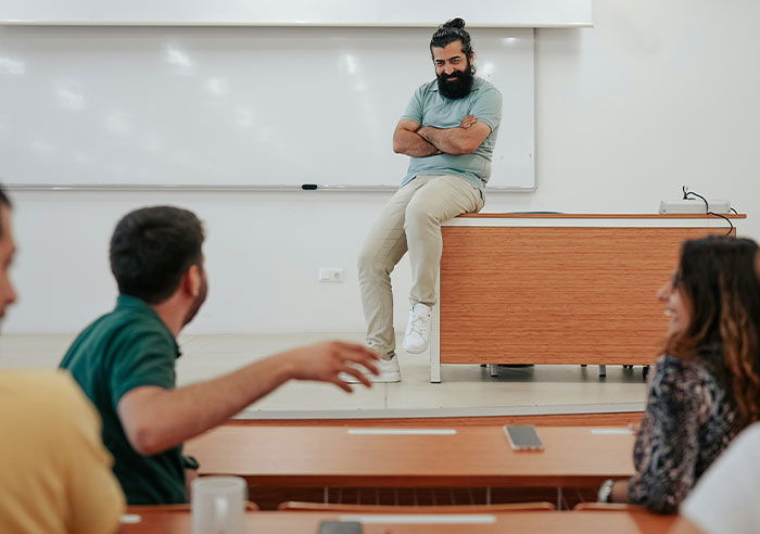 Man with beard and casual clothes teaching students in a classroom sparking eye-opening spoiled moments discussion.