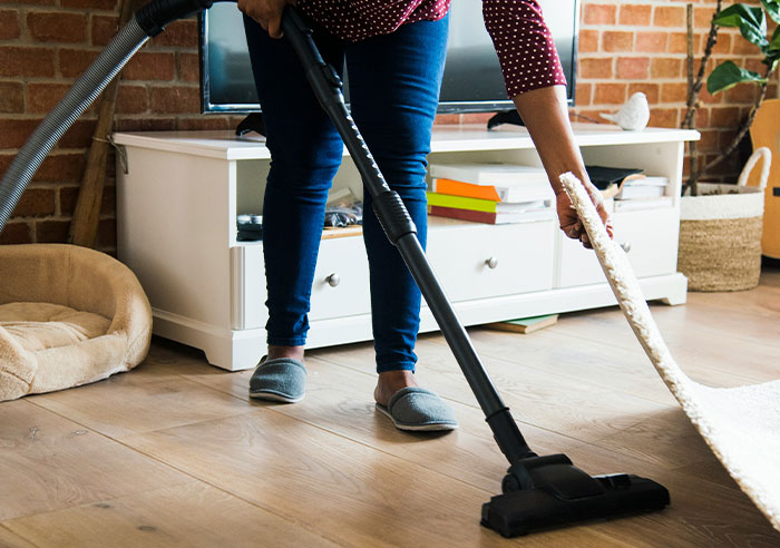 Person vacuuming hardwood floor while lifting a rug, illustrating eye-opening moments that made people realize they were spoiled.