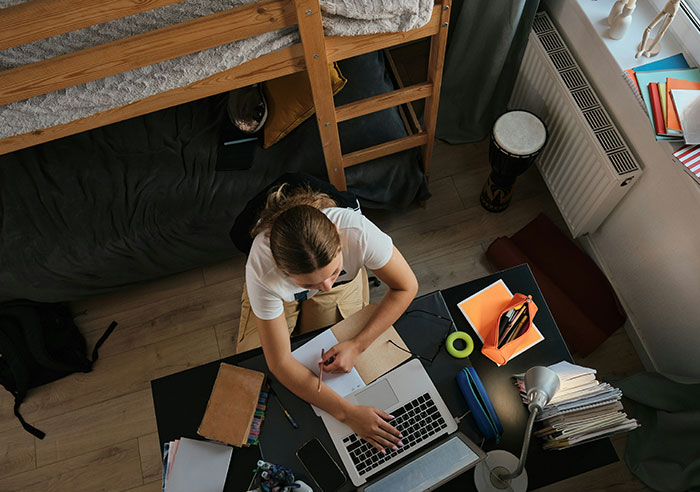 Teen working on laptop at a cluttered desk in a small room, highlighting moments that made people realize they were spoiled.