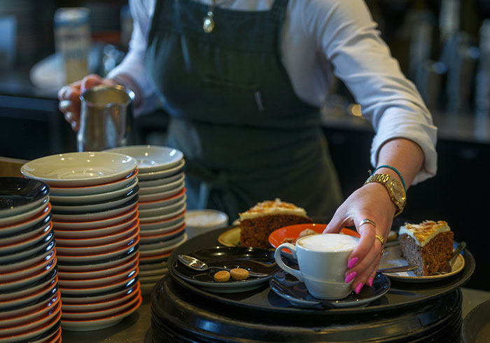 Barista serving coffee and cake with stacked plates in café, illustrating moments that made people realize they were spoiled.