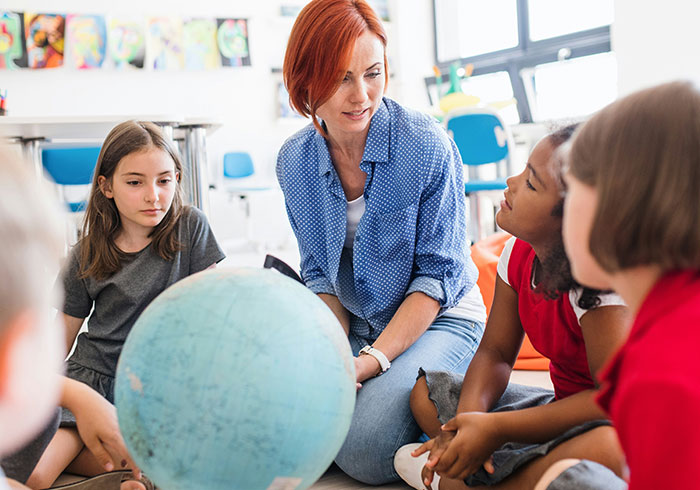Teacher and diverse kids sitting on floor around globe during an eye-opening moment about being truly spoiled.