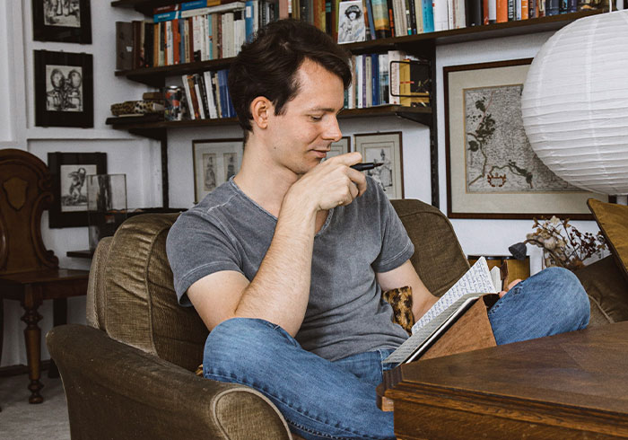 Young man reading a book in a cozy room filled with books, reflecting on eye-opening moments of being spoiled.