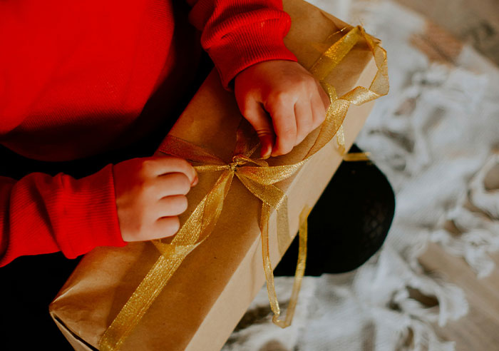 Child in red sweater untying a gold ribbon on a wrapped gift, illustrating moments that made people realize they were spoiled.
