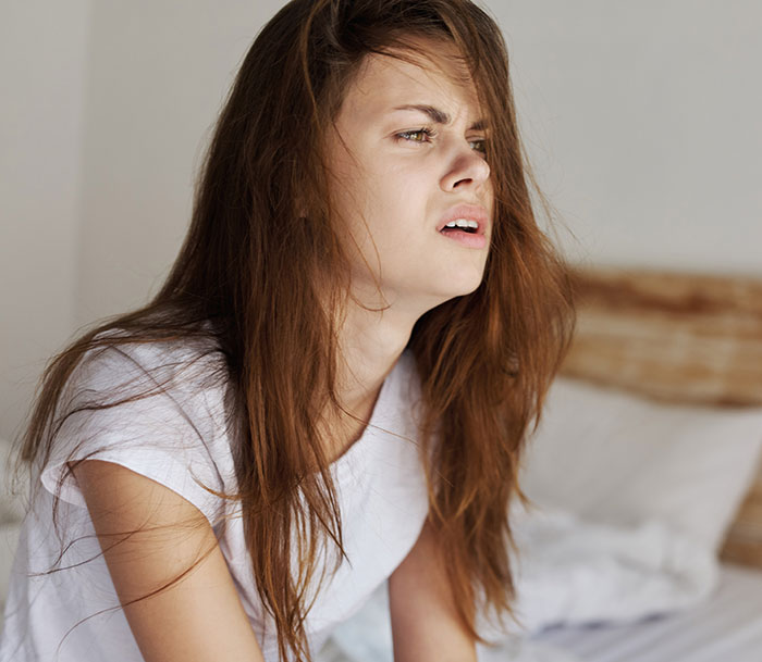 Teen girl with long hair looking confused and upset while sitting on a bed, reflecting a creepy step-sister hair cutting incident.