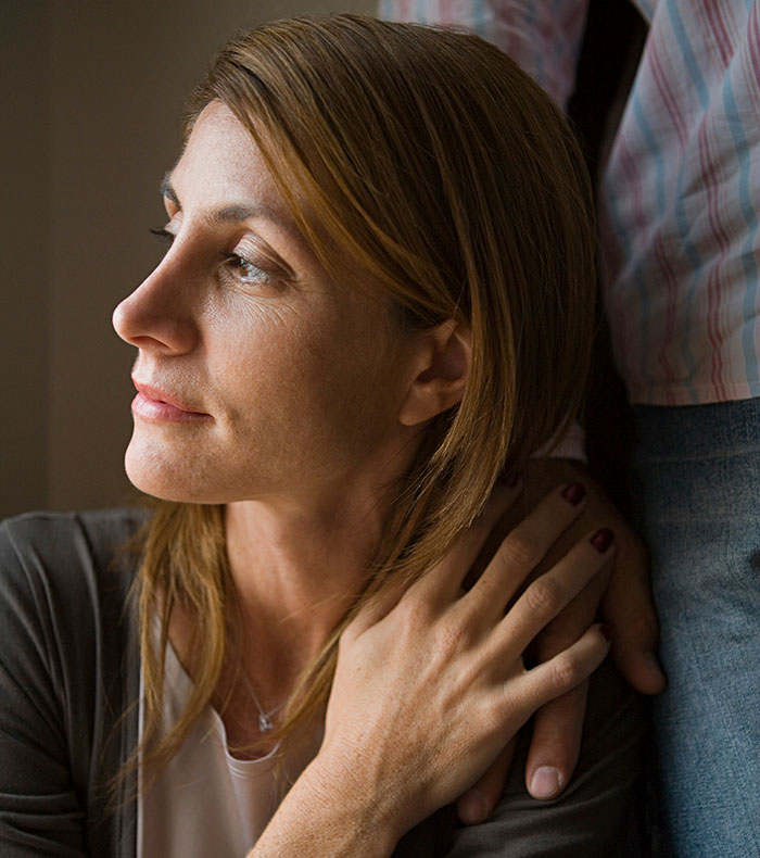 Woman looking thoughtfully while holding husband's hand, reflecting struggle with chemotherapy and family conflict.