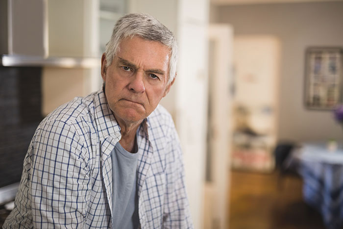 Angry older man in a checked shirt sitting indoors, depicting refusal and conflict over chemotherapy treatment.