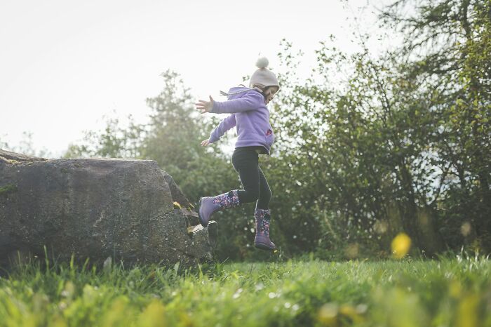 Child in purple jacket and boots jumping off a rock, illustrating mystery and unexplained phenomenon in nature.