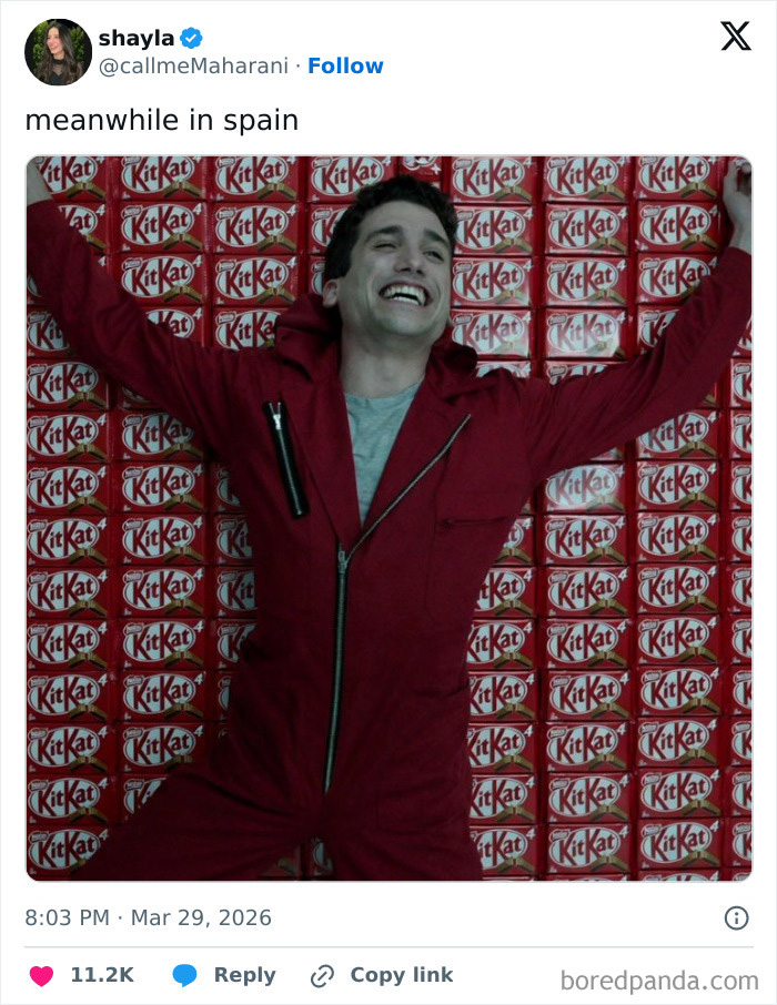 Man in red jumpsuit smiling and spreading arms lying on a large stack of KitKat bars, related to KitKat theft responses.