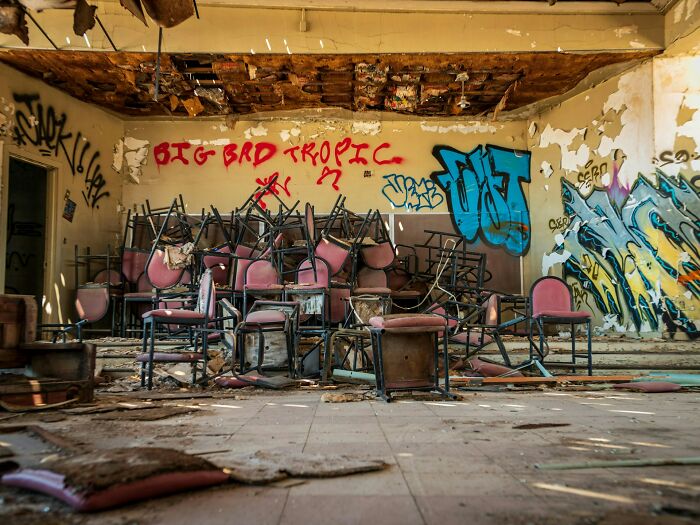 Abandoned room with broken chairs and graffiti on walls, a chilling setting for urban explorers dropping their flashlights.