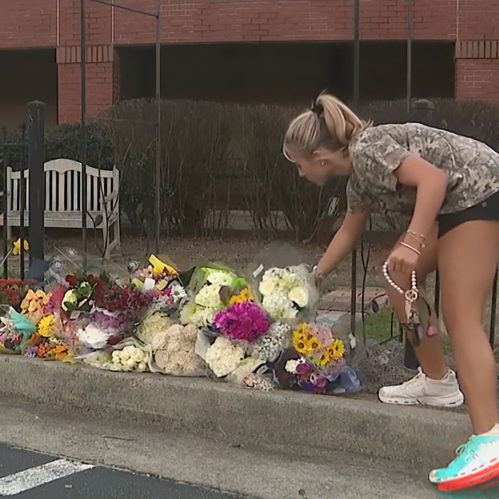 Young woman placing flowers at a roadside memorial honoring a high school teacher who lost his life in a prank gone wrong.