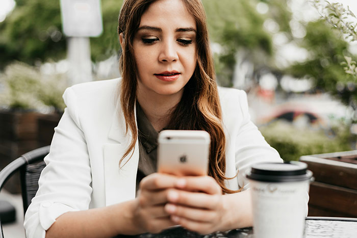 Woman with a goofy smile checking her phone outside, reflecting on her husband's horrible cheating behavior.