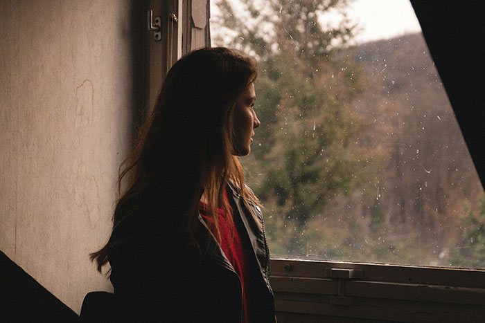 Woman looking out a window, reflecting sadly on her innocent goofy joke revealing her horrible cheating husband.