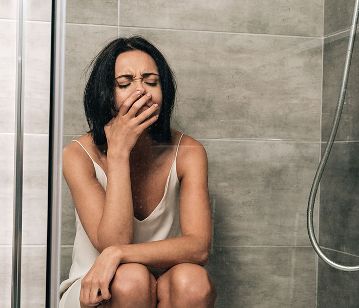Woman sitting in a shower cubicle looking distressed, reflecting on her husband's horrible cheating behavior.