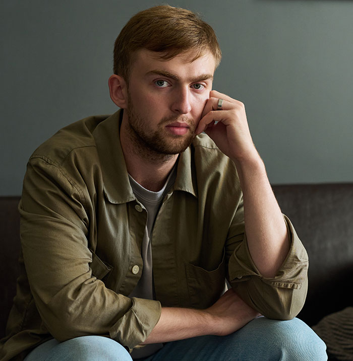 Young man with a serious expression sitting indoors, reflecting themes of horrible cheating jerk in relationships.