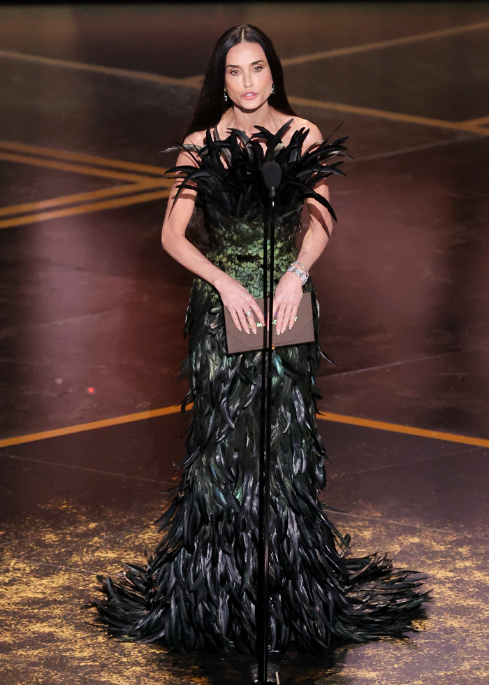 Demi Moore wearing a black feathered gown on stage at the Oscars, styled with a troubling scary detail revealed by a stylist.
