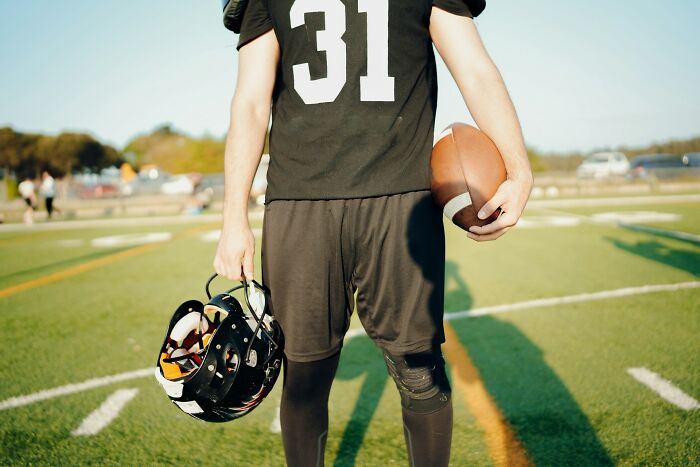 Football player standing on field holding helmet and ball, symbolizing moments people destroyed their own lives in an instant.